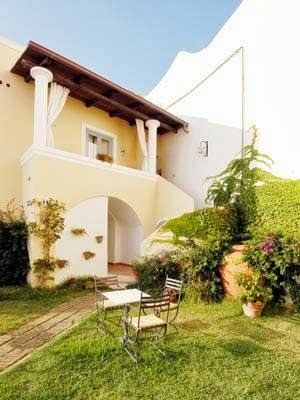 The hotel's charming yellow exterior facade with a lush garden courtyard featuring seating areas and climbing ivy.