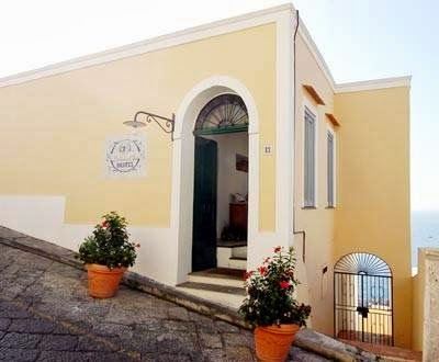 The charming yellow exterior entrance of Hotel la Casa sul Mare features a rounded arched doorway with potted flowers and stone steps.