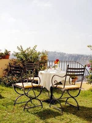 An outdoor dining setup with a round table and chairs on a manicured lawn overlooking a scenic hillside landscape.